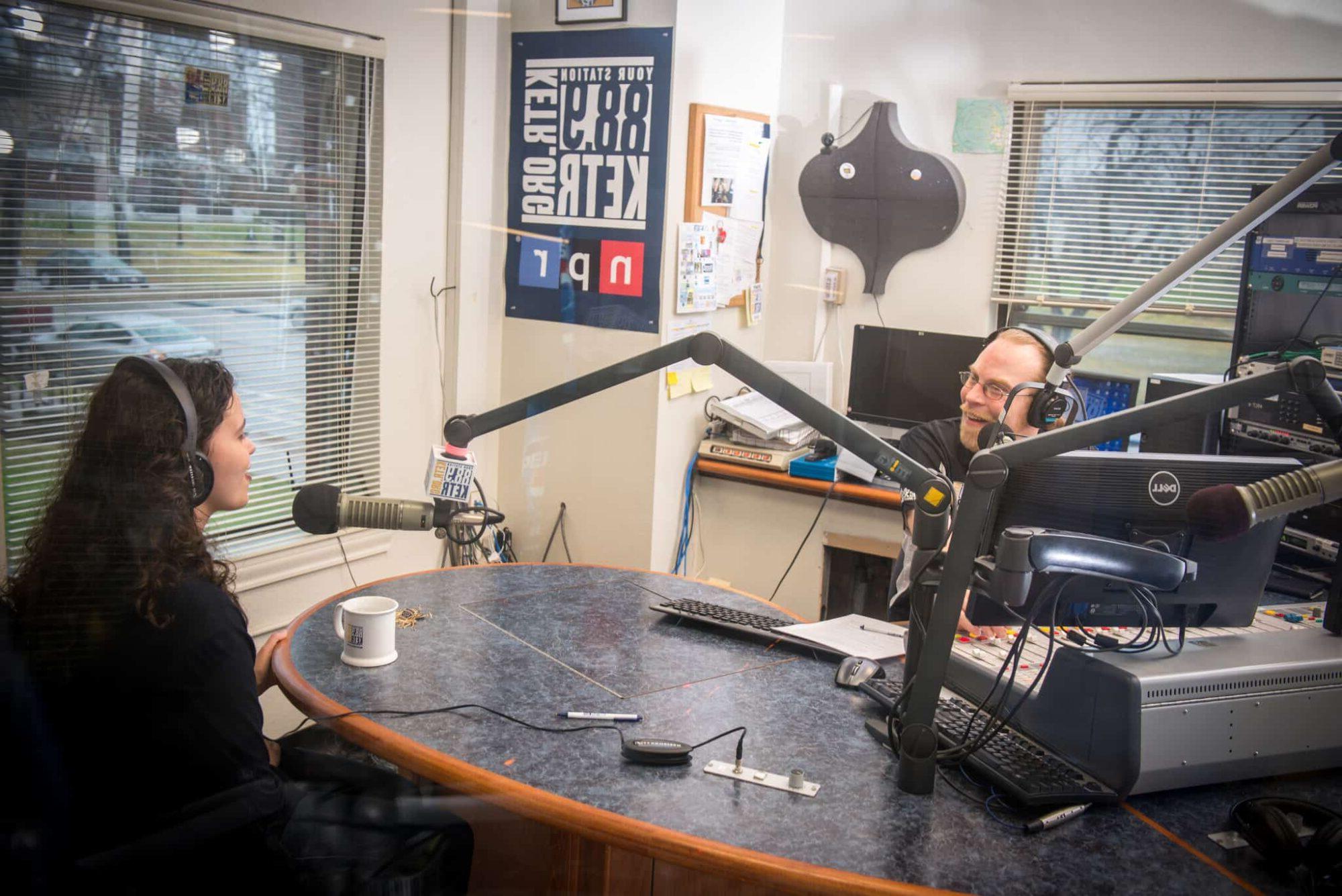 A man is speaking to a young female at the KETR radio studio.